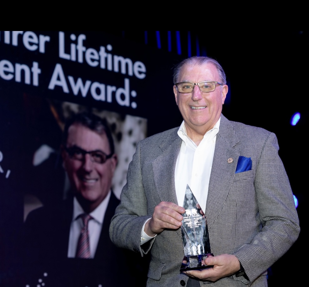 Clark Dumont in a sportcoat holding a crystal award.